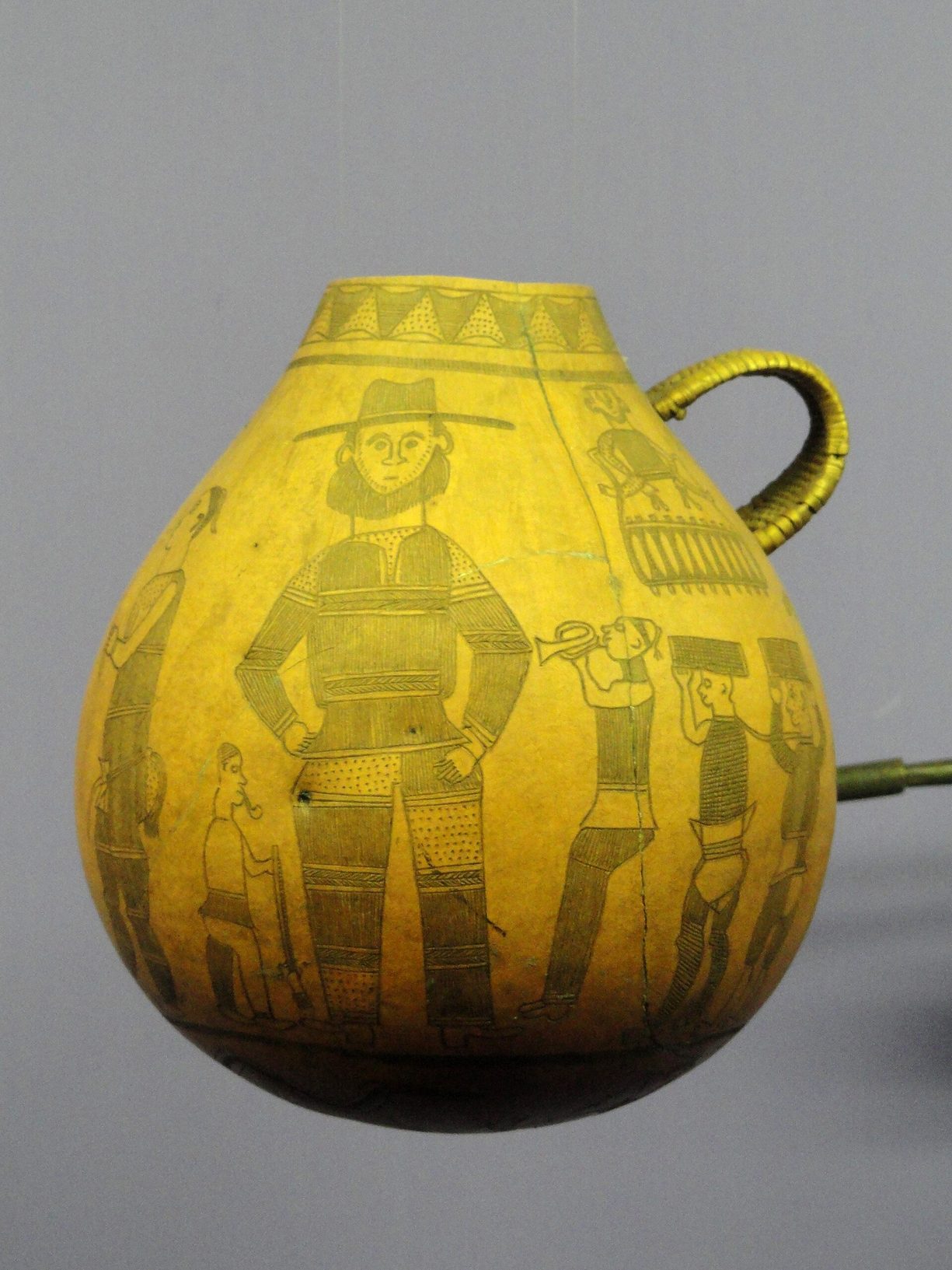 Calabaza azande grabada con figuras de europeos: un hombre barbudo con sombrero, un cornetín y porteadores con cargas sobre la cabeza