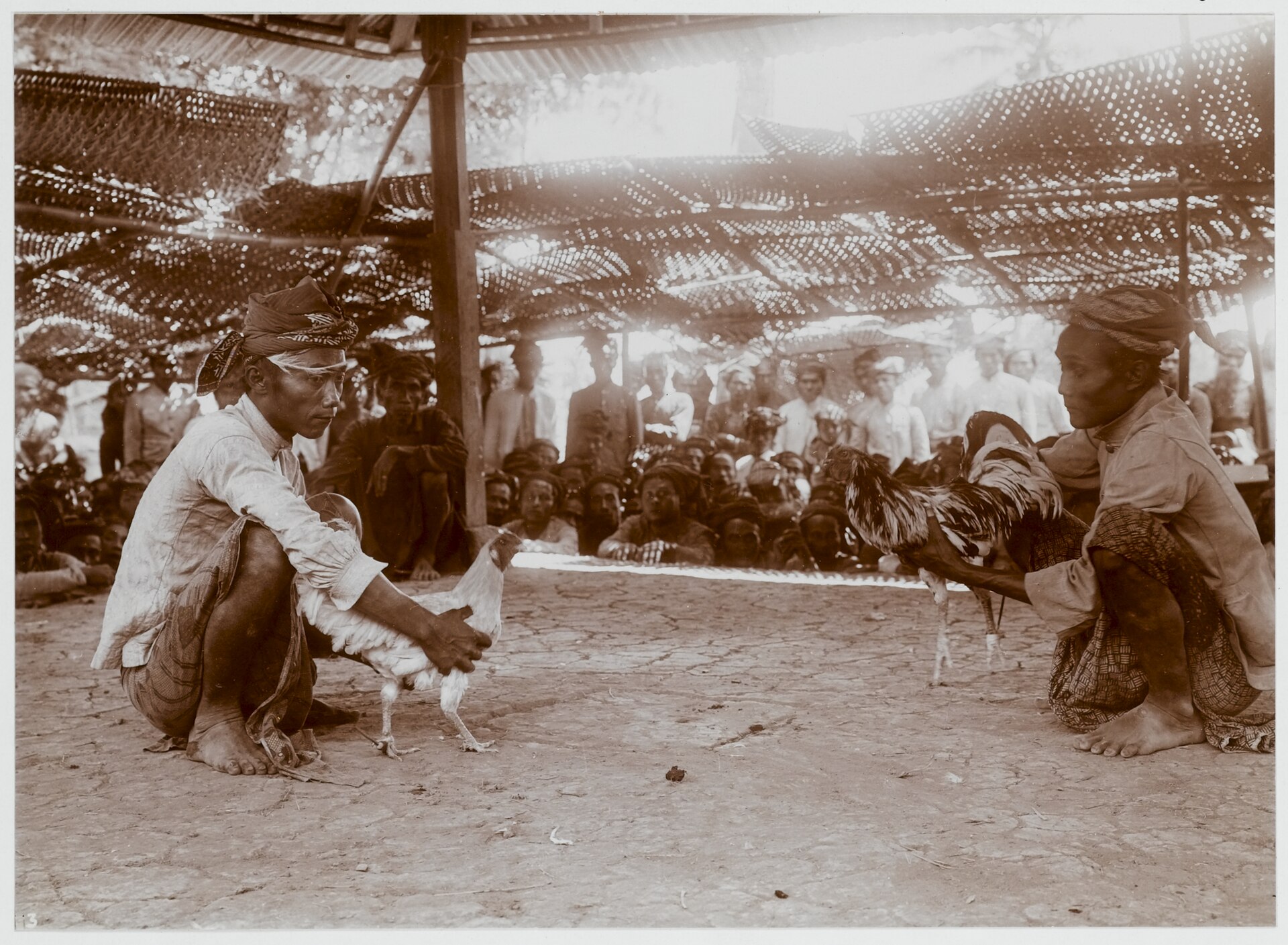 Fotografía antigua de espectadores de pie formando un corro en torno a la arena de una pelea de gallos