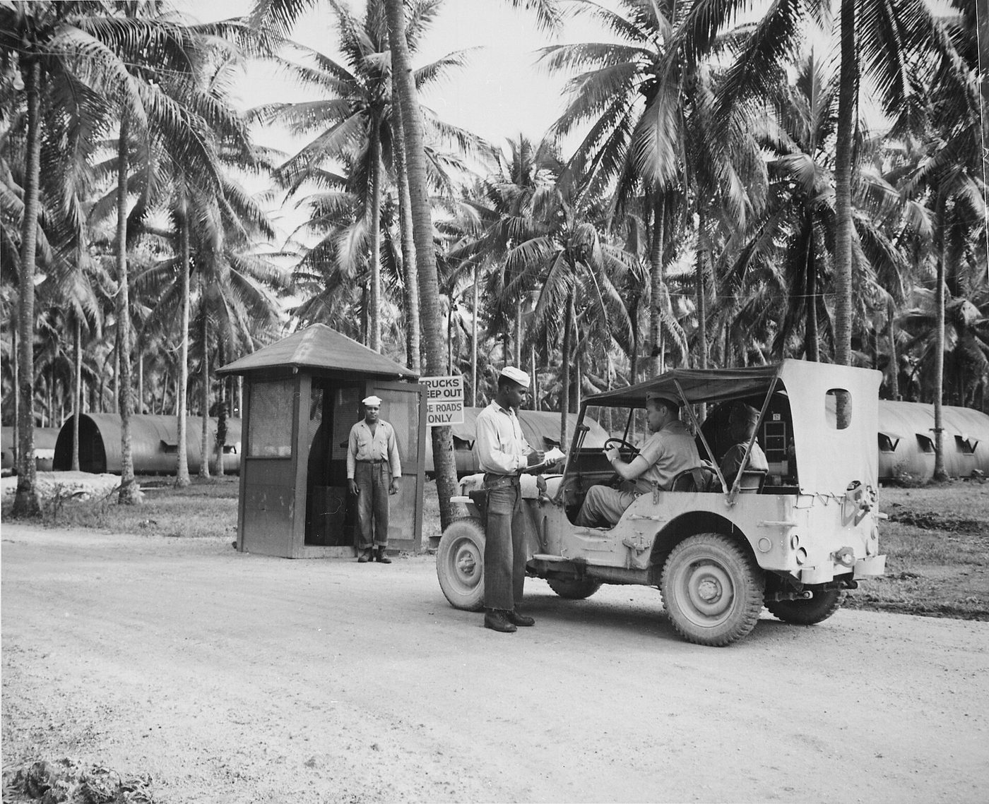 Jeep detenido ante la garita de entrada a la base naval estadounidense de Espíritu Santo entre palmeras y barracones semicilíndricos