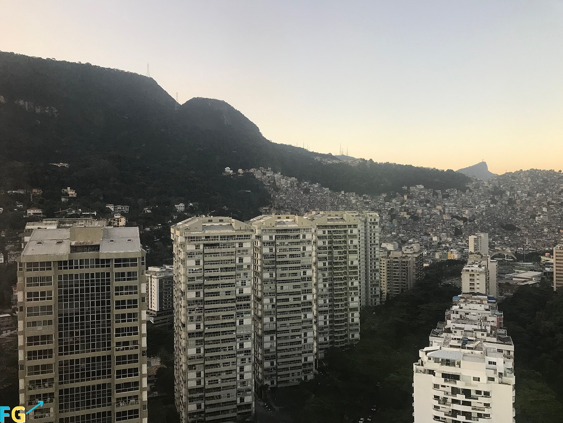 Fotografía en color al atardecer de torres de apartamentos altas en primer plano y, detrás, una ladera cubierta de casas pequeñas de ladrillo hasta la cima del monte