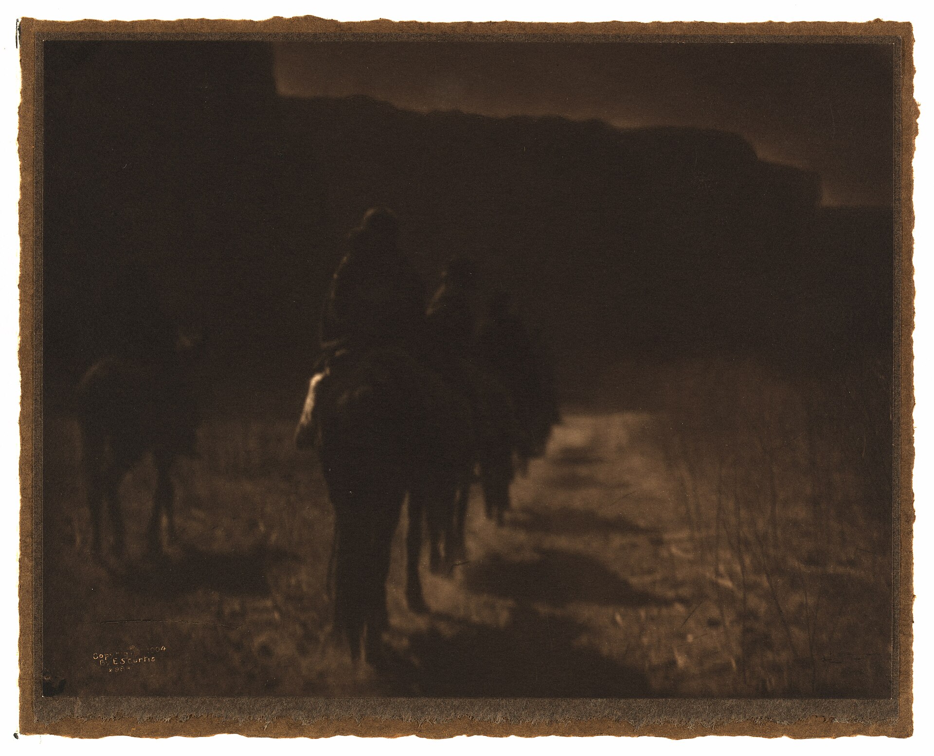 Fotograbado muy oscuro en tonos sepia de un grupo de jinetes que se alejan en fila por un desfiladero en penumbra