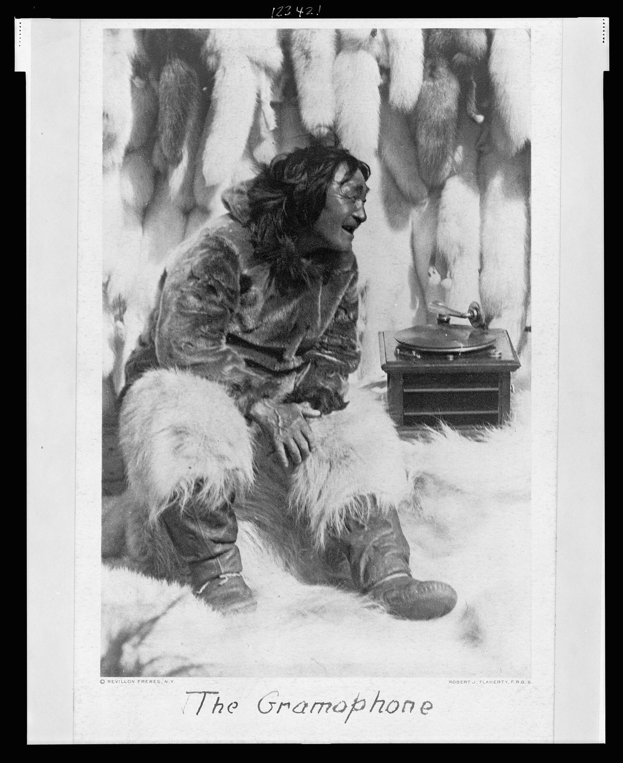 Fotograbado de un hombre con parka de piel arrodillado, sonriendo con la boca abierta ante un gramófono portátil, bajo el rótulo The Gramophone