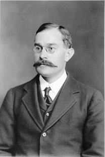 Retrato fotográfico de un hombre joven con gafas y bigote, de estudio