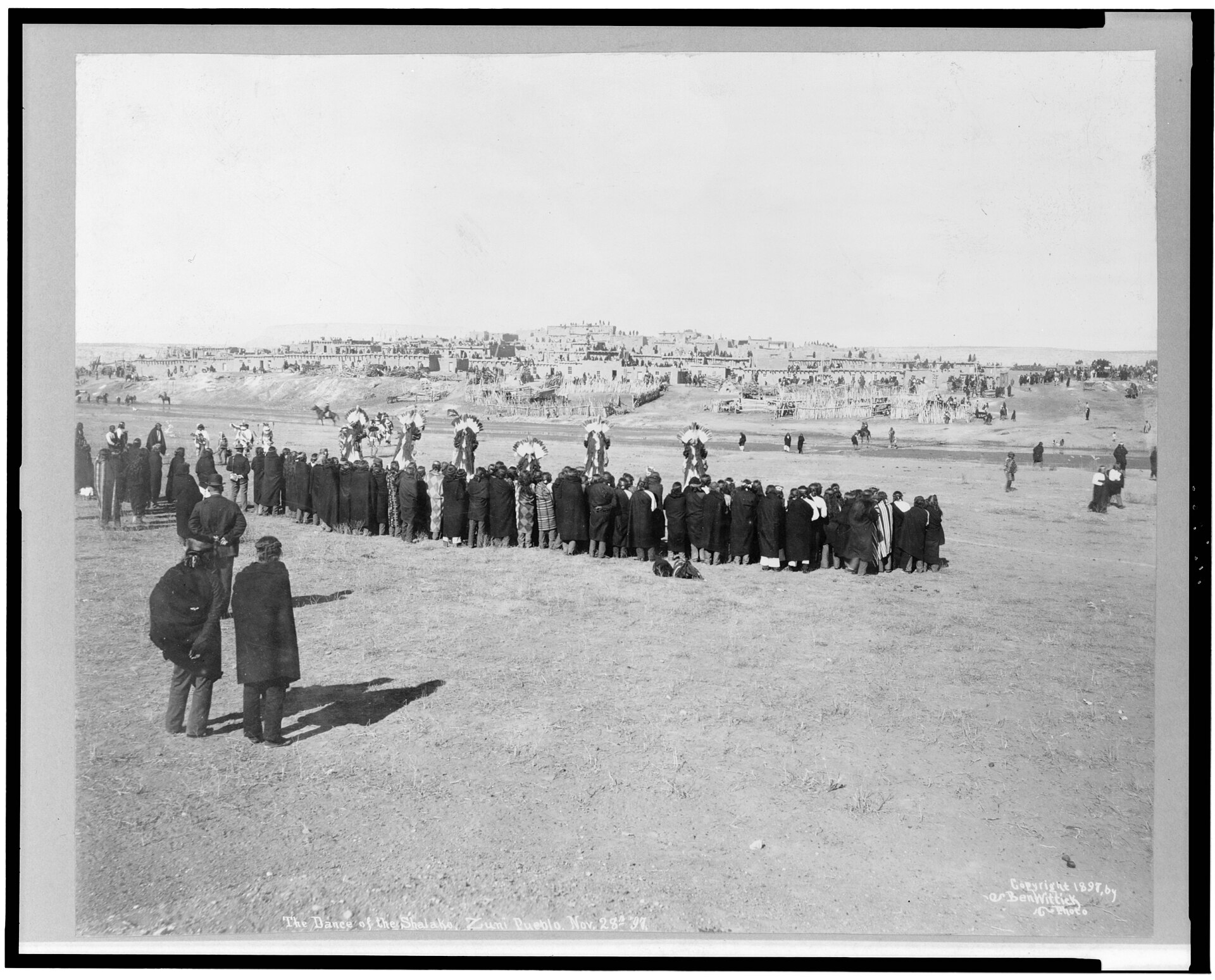 Fotografía panorámica de 1897 de una larga fila de personas congregadas en una explanada junto a un poblado