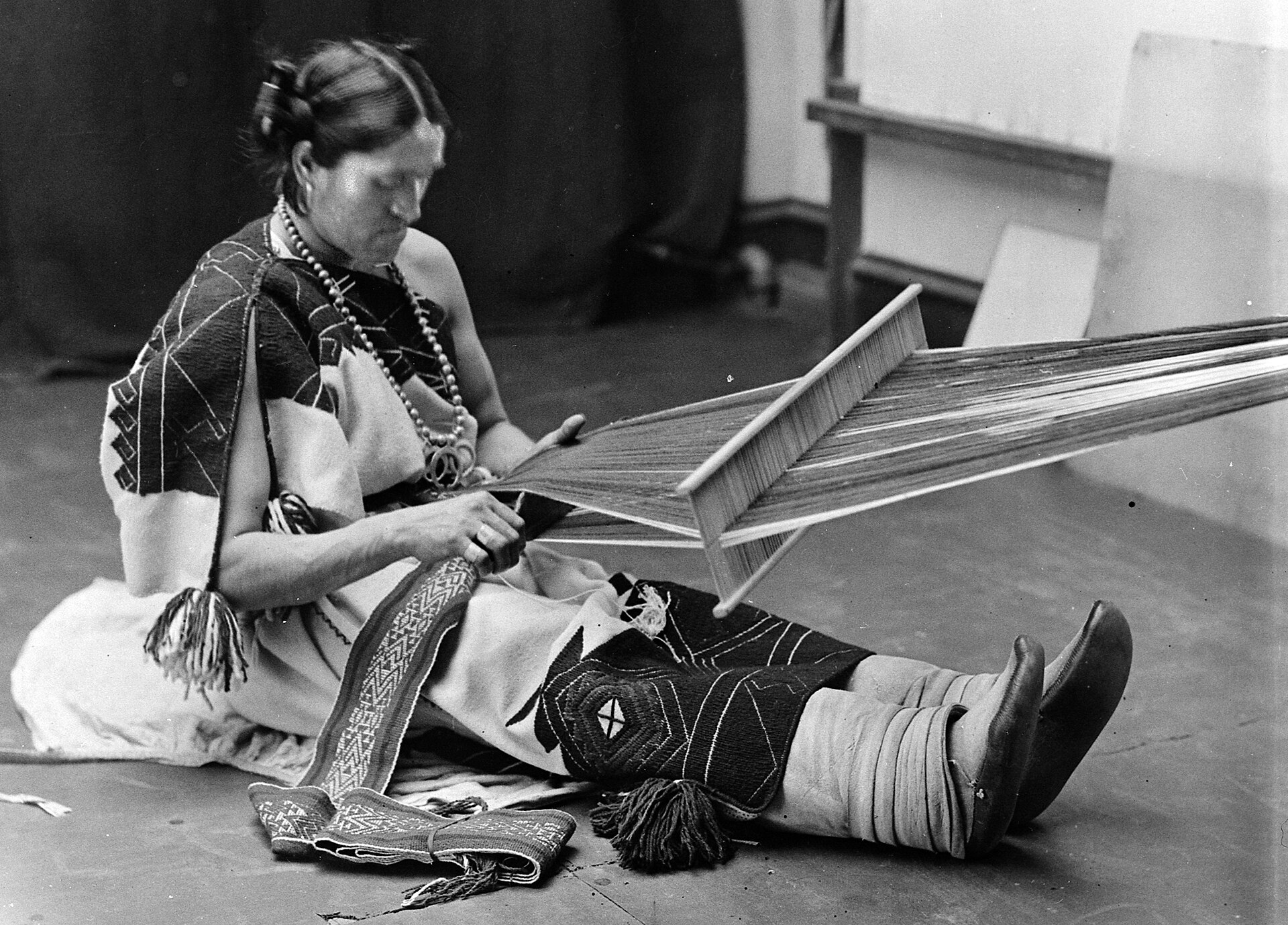 Fotografía del siglo XIX de una persona sentada en el suelo trabajando en un telar de urdimbre tensada
