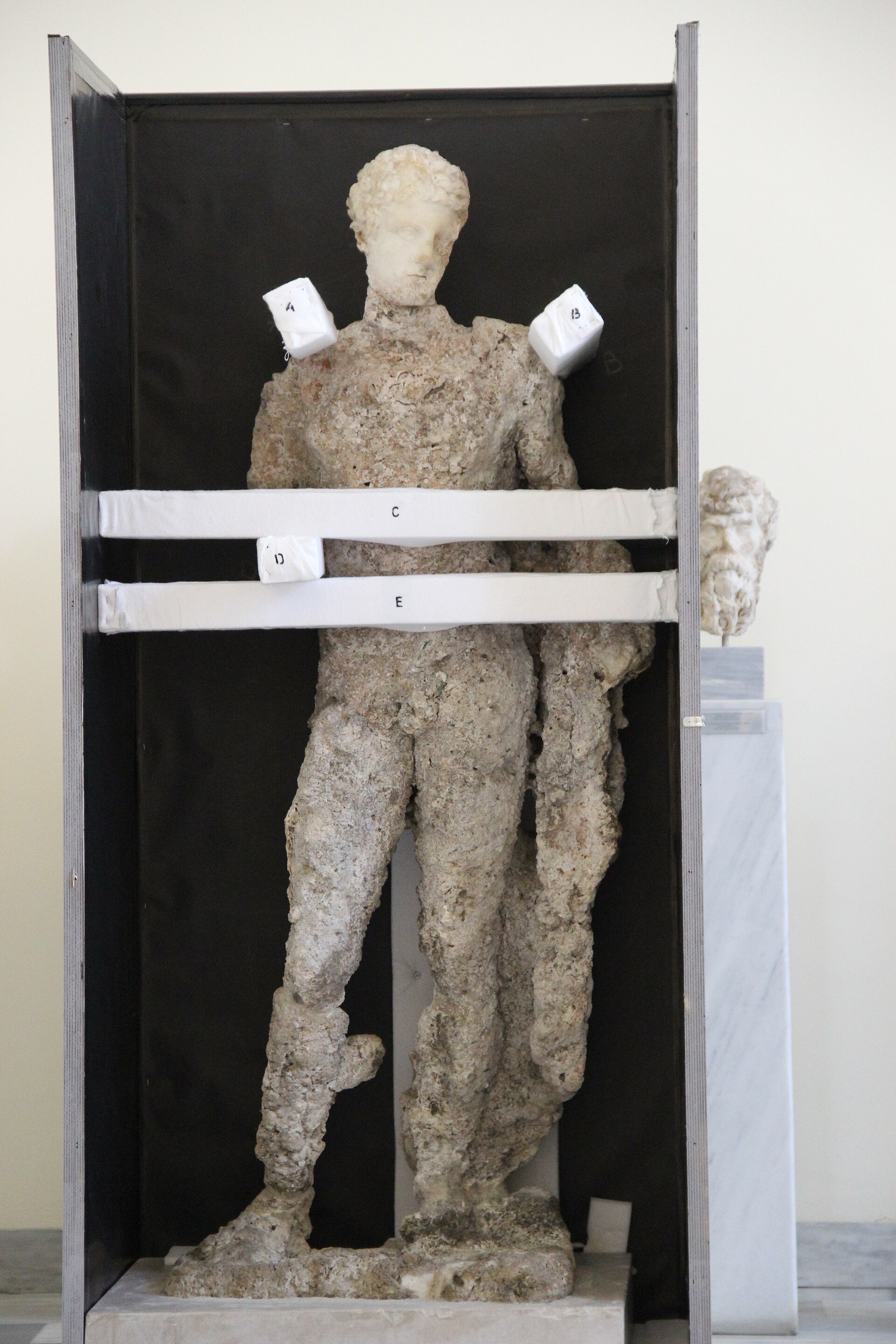Estatua de mármol de un joven desnudo, de pie, con el peso del cuerpo cargado sobre una pierna