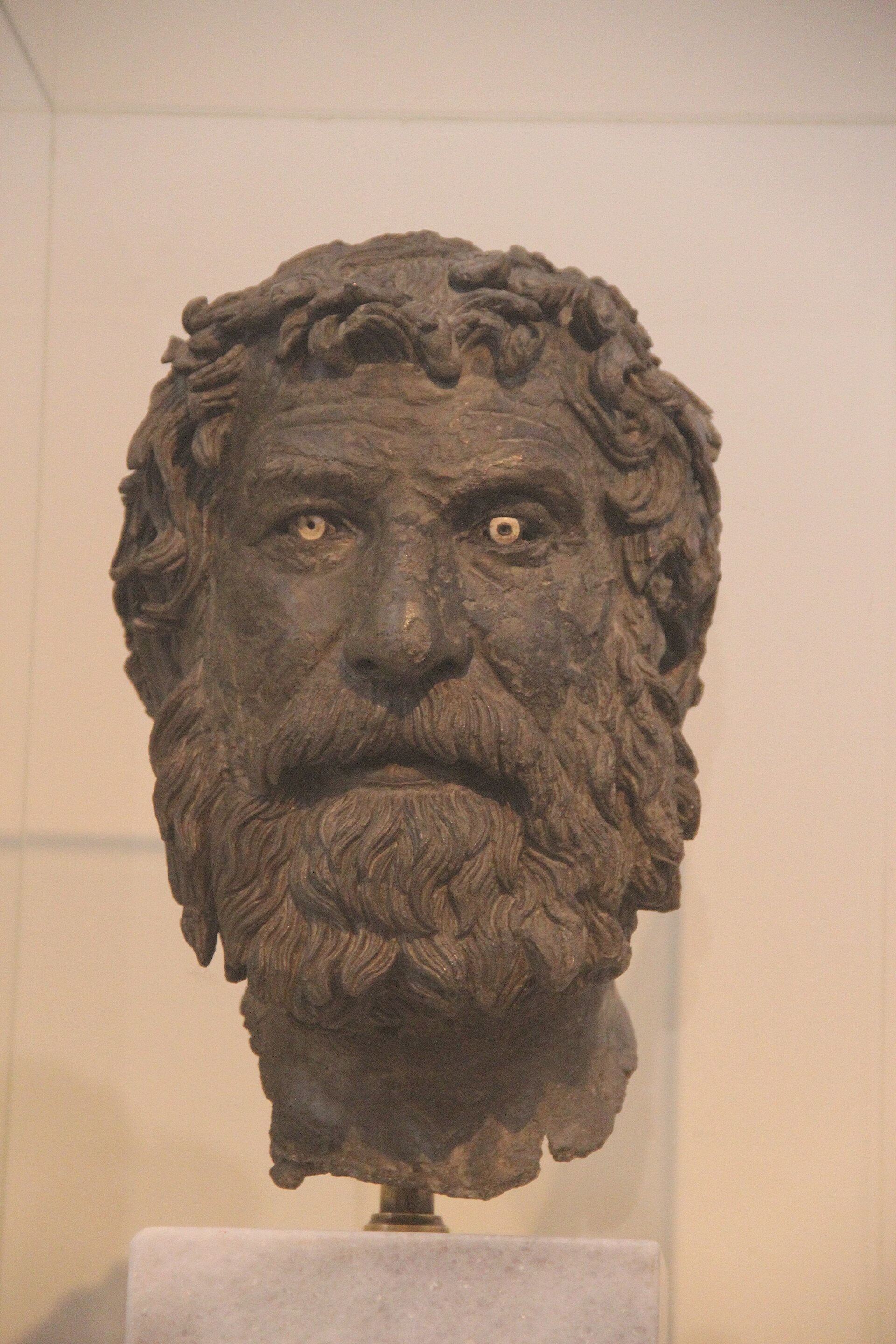 Cabeza de bronce de un hombre barbado con expresión seria, pátina verdosa
