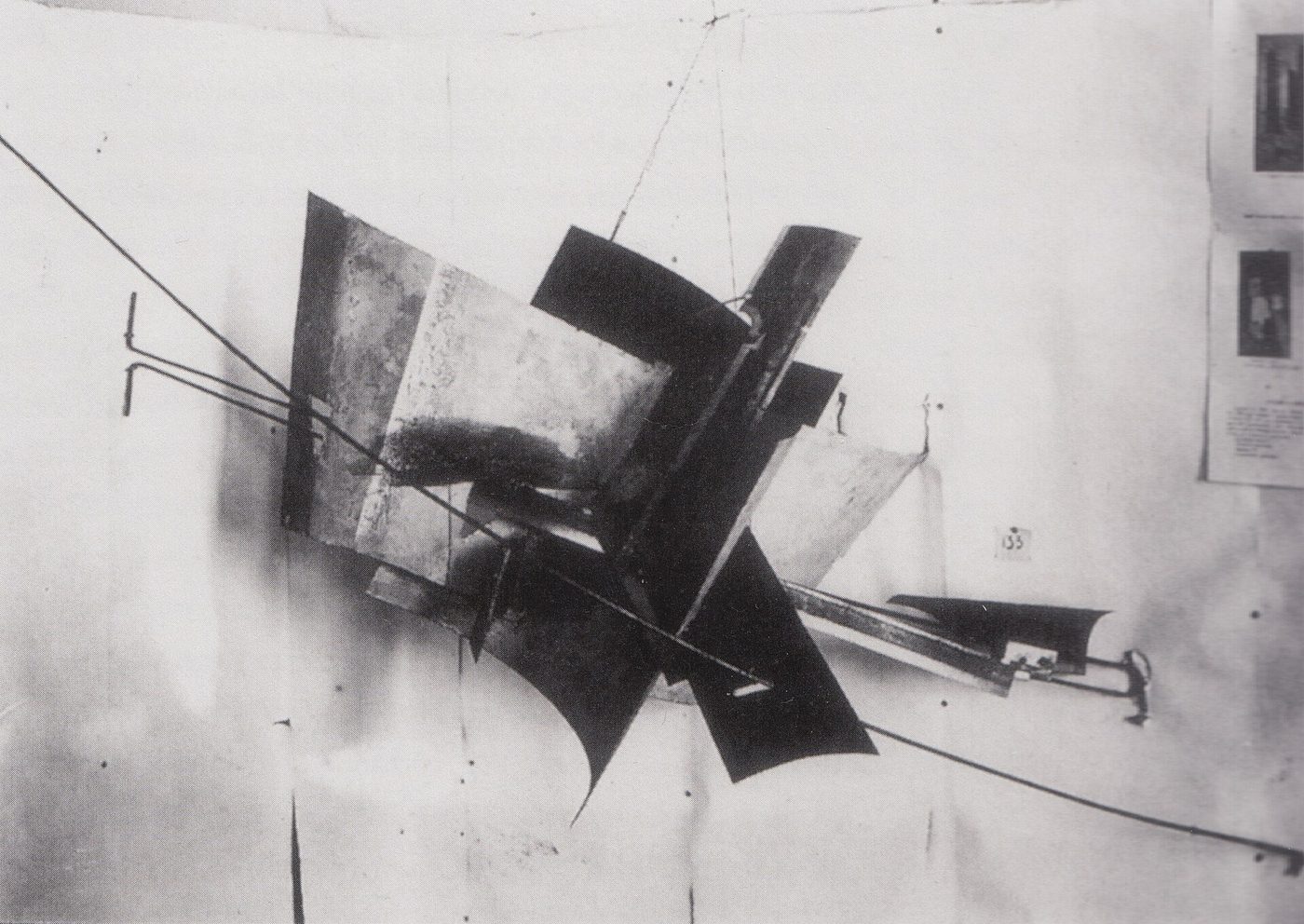 Fotografía en blanco y negro de una construcción de chapas metálicas curvas y planas suspendida con cables en la esquina de una sala