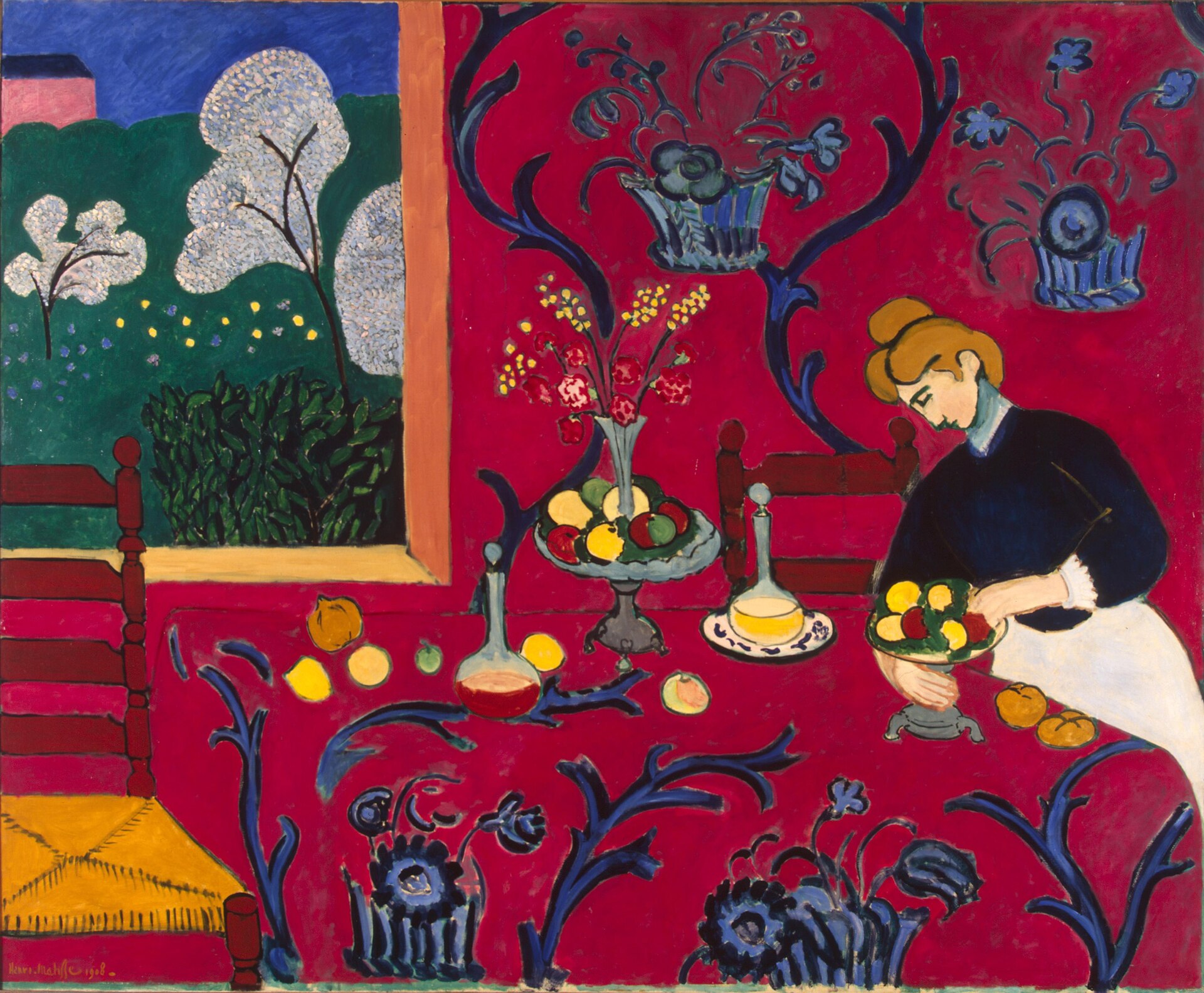 Pintura de un comedor donde la pared y el mantel son de un rojo intenso cubierto de arabescos azules, una mujer arregla fruta en la mesa y una ventana muestra un jardín verde