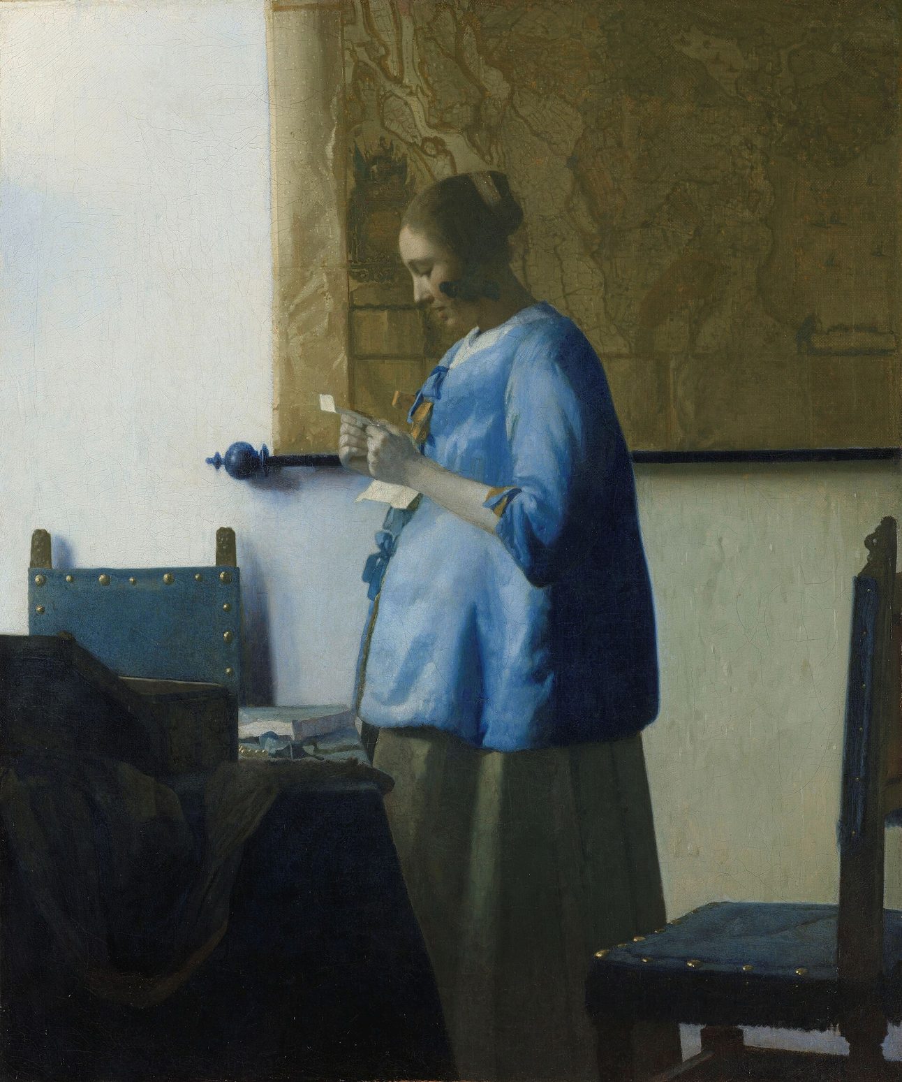 Mujer de azul leyendo una carta, de Vermeer: una mujer de pie junto a una mesa, de perfil, con chaqueta azul, ante un mapa colgado en la pared