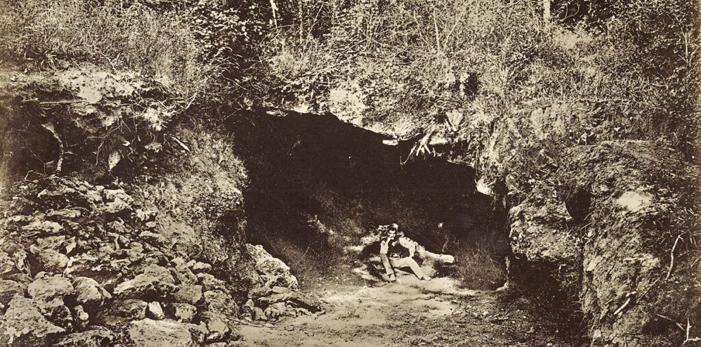 Fotografía antigua de una ladera con una oquedad excavada en la roca y montones de tierra removida al pie