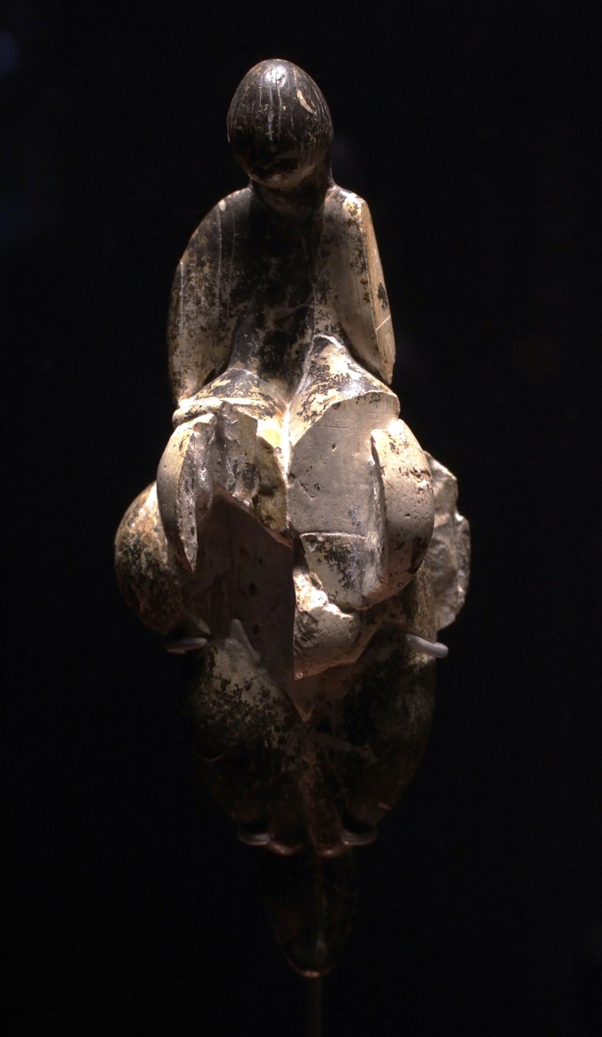Figurilla de marfil alargada, con formas ovoides superpuestas, cabeza pequeña sin rasgos y volúmenes simétricos, iluminada sobre fondo negro