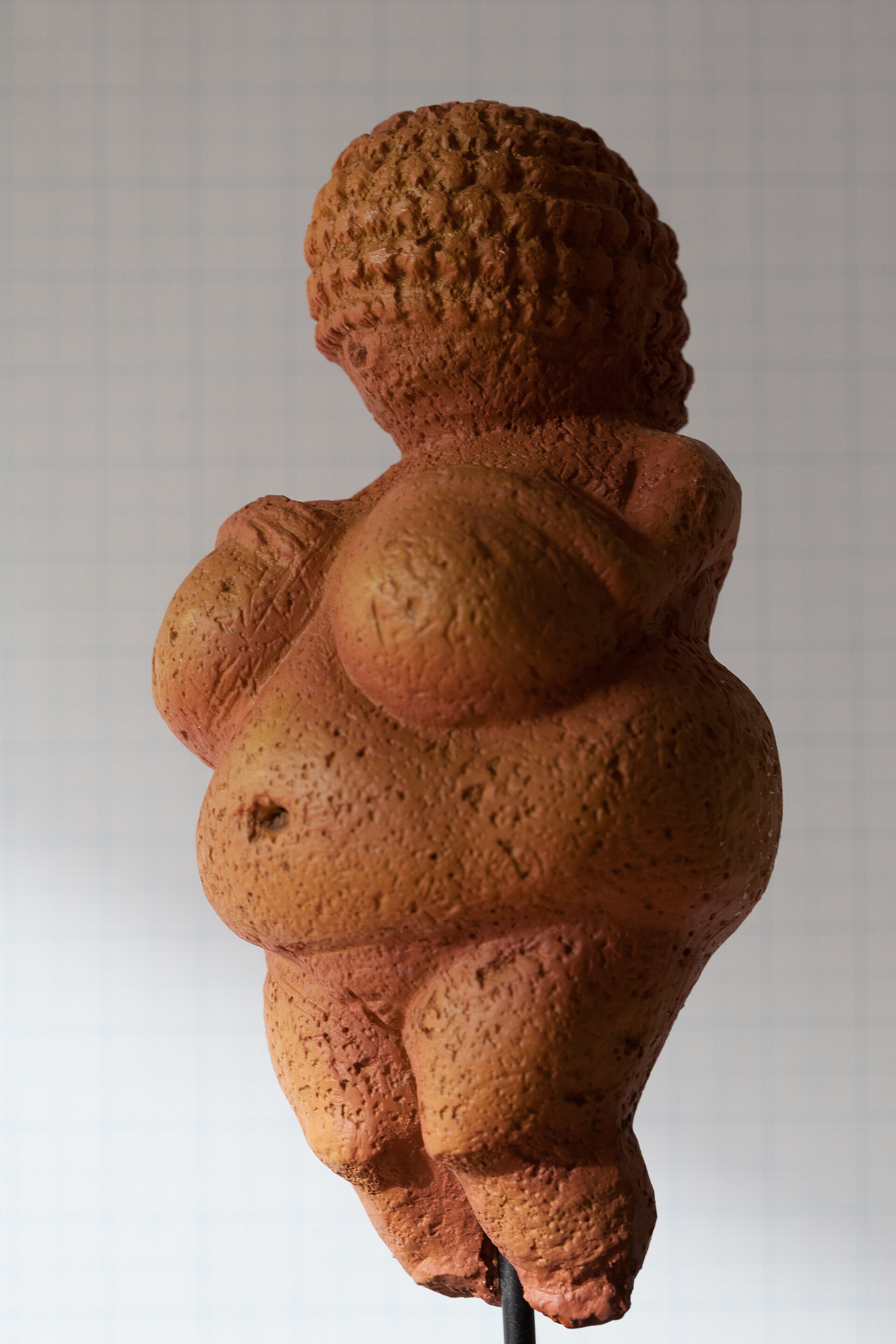 Réplica de la Venus de Willendorf sobre papel milimetrado: figura femenina de pechos y vientre voluminosos, brazos delgados sobre los pechos y cabeza cubierta por un tejido en espiral, sin rostro