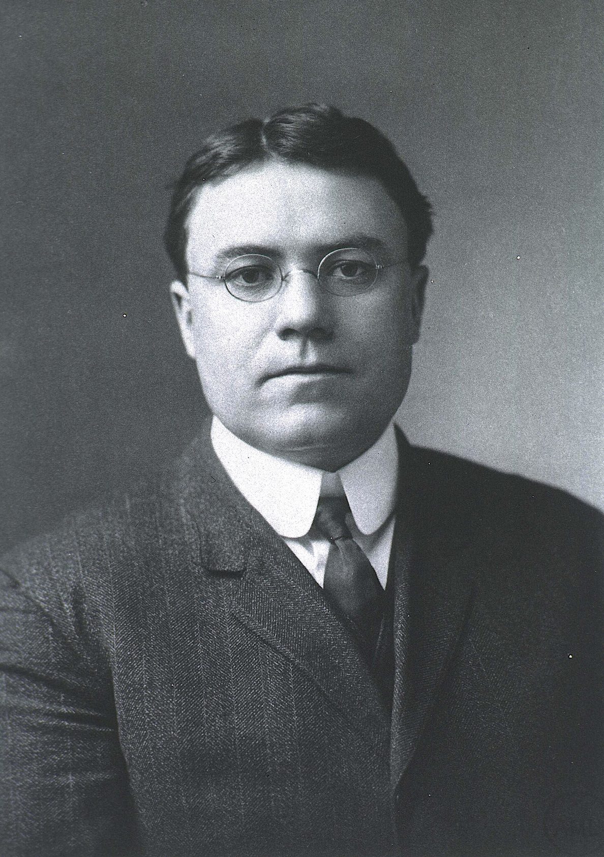 Fotografía en blanco y negro de un hombre joven con traje y gafas, de principios del siglo XX