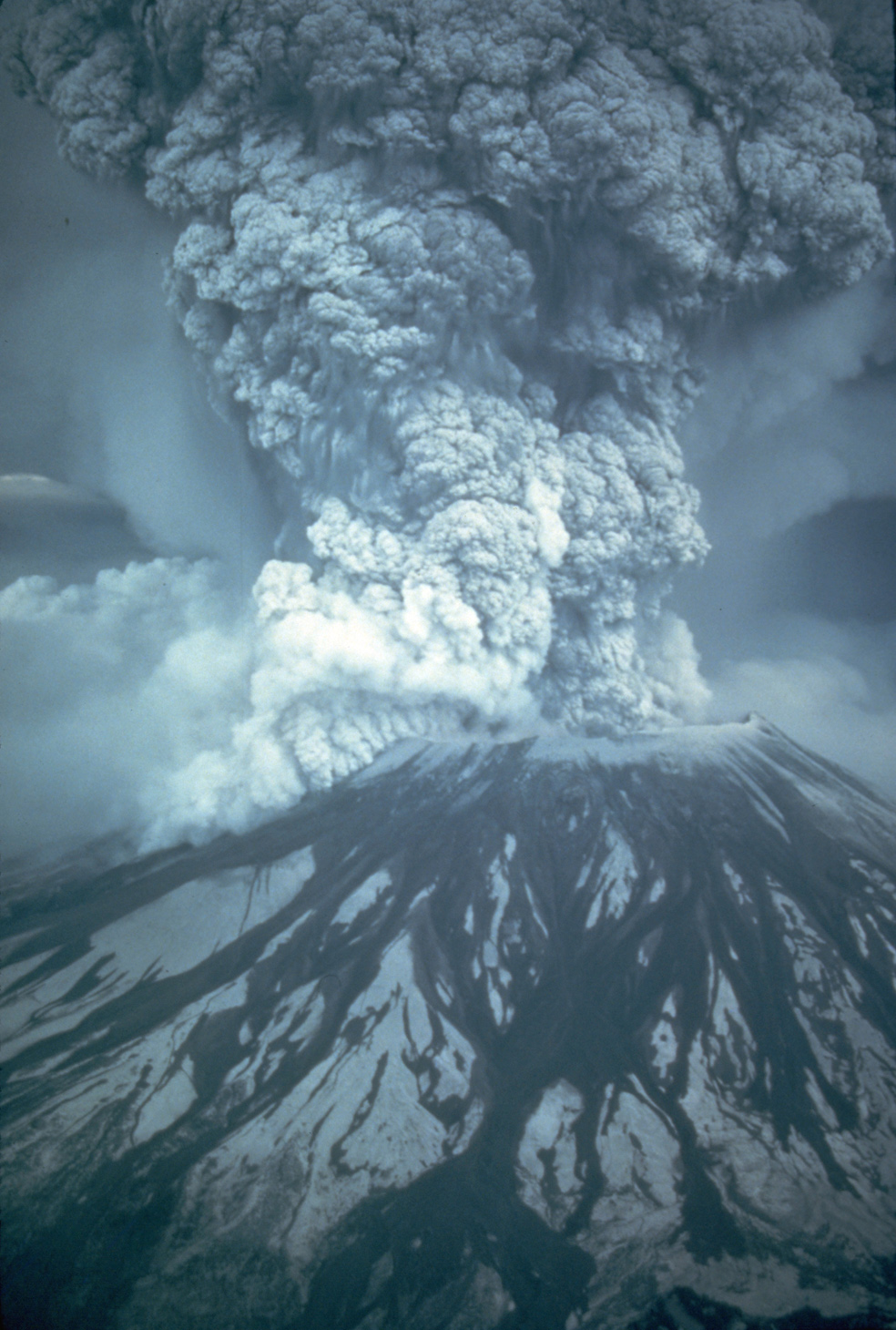 Fotografía de una gran erupción volcánica con una columna de ceniza gris que se eleva sobre la montaña