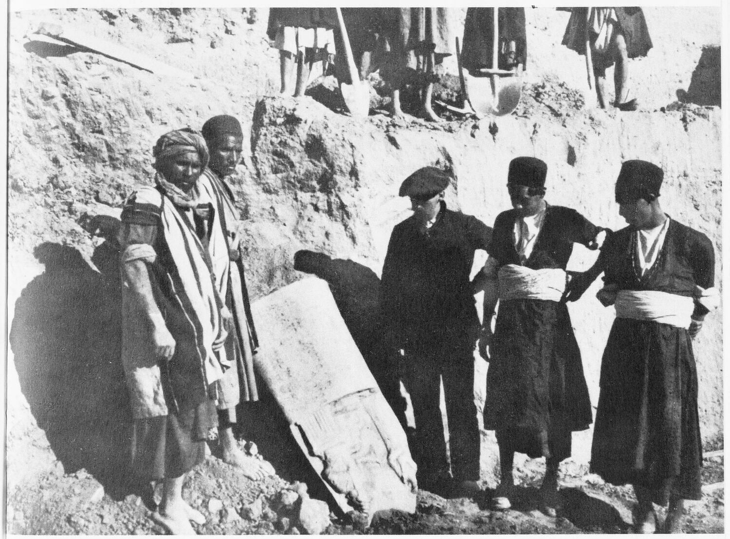 Fotografía antigua en blanco y negro de varios hombres con ropa de trabajo junto a un gran bloque de piedra en una excavación