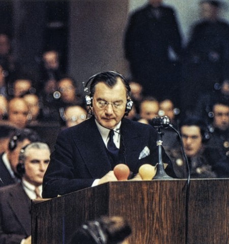 Fotografía en color de un hombre de traje oscuro que lee de pie tras un atril de madera con micrófonos, con auriculares, ante un público también con auriculares