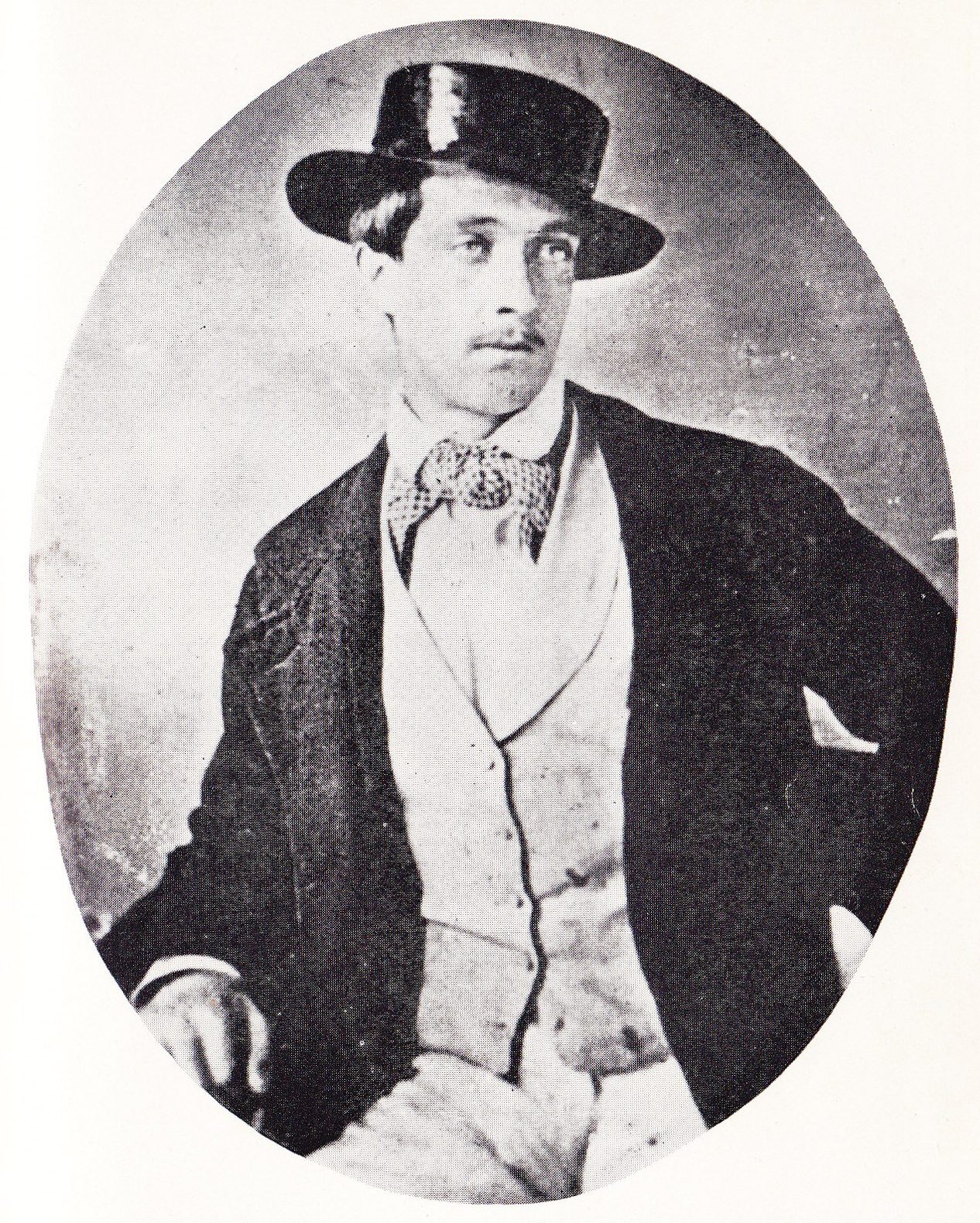 Retrato fotográfico ovalado de un joven delgado con sombrero de copa baja, chaqueta oscura y corbata de lazo