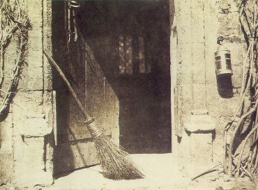 Calotipo de 1844 con una puerta entreabierta en un muro de piedra, una escoba apoyada en la jamba y un farol colgado