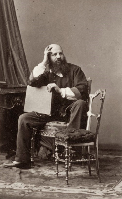 Retrato fotográfico del siglo XIX de un hombre barbudo sentado junto a una silla, con la mano en la sien y actitud pensativa