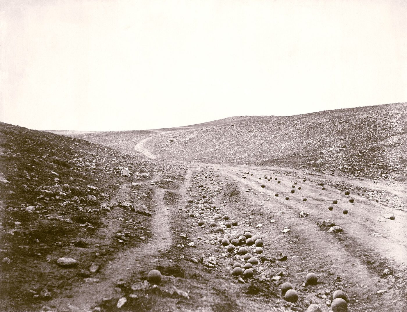 Fotografía de 1855 de un camino de tierra entre laderas peladas, cubierto de balas de cañón esféricas