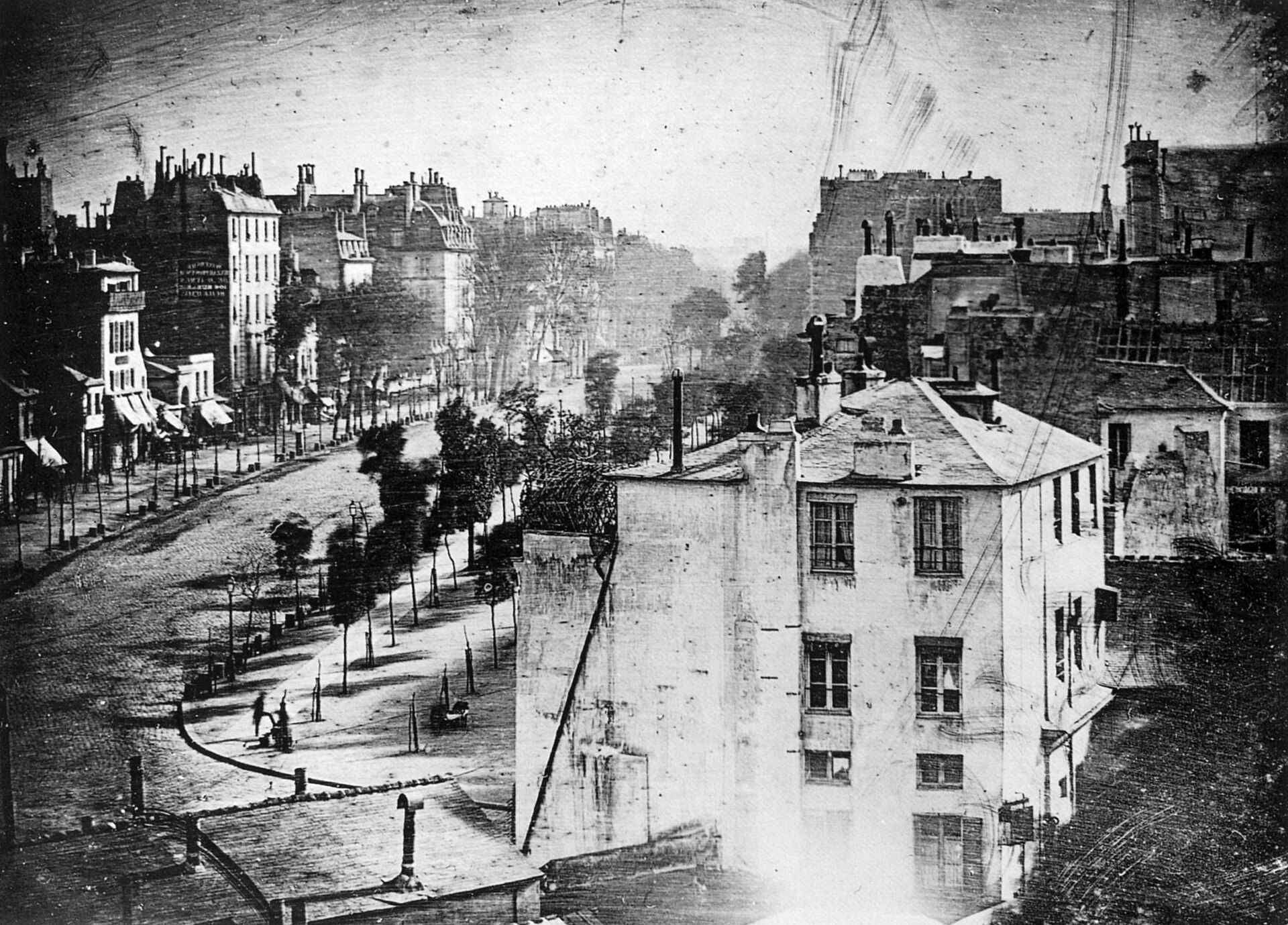 Daguerrotipo de 1838 de una amplia avenida parisina con edificios y árboles, vacía de tráfico salvo dos figuras diminutas en la acera inferior izquierda