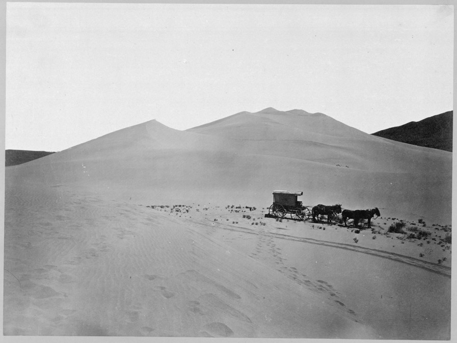 Fotografía de 1867 de una gran duna vacía con un carro tirado por mulas al pie y rodadas marcadas en la arena