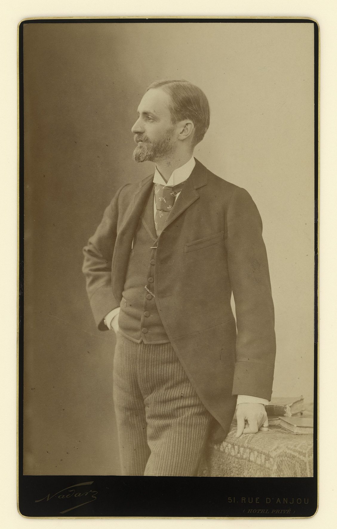 Retrato de estudio de George Eastman de pie, con traje oscuro y las manos en los bolsillos