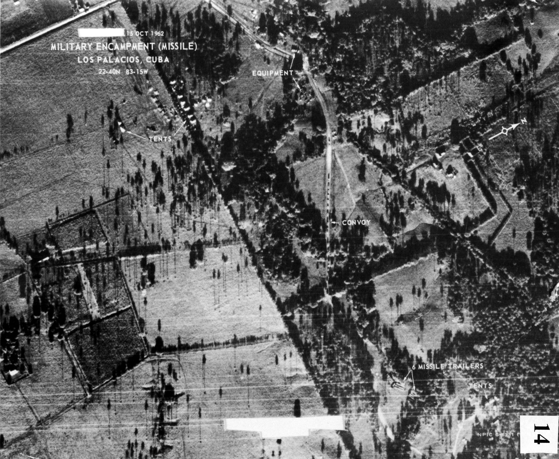 Fotografía aérea en blanco y negro de un terreno con árboles y caminos, con rótulos que señalan tiendas, vehículos y un campamento militar