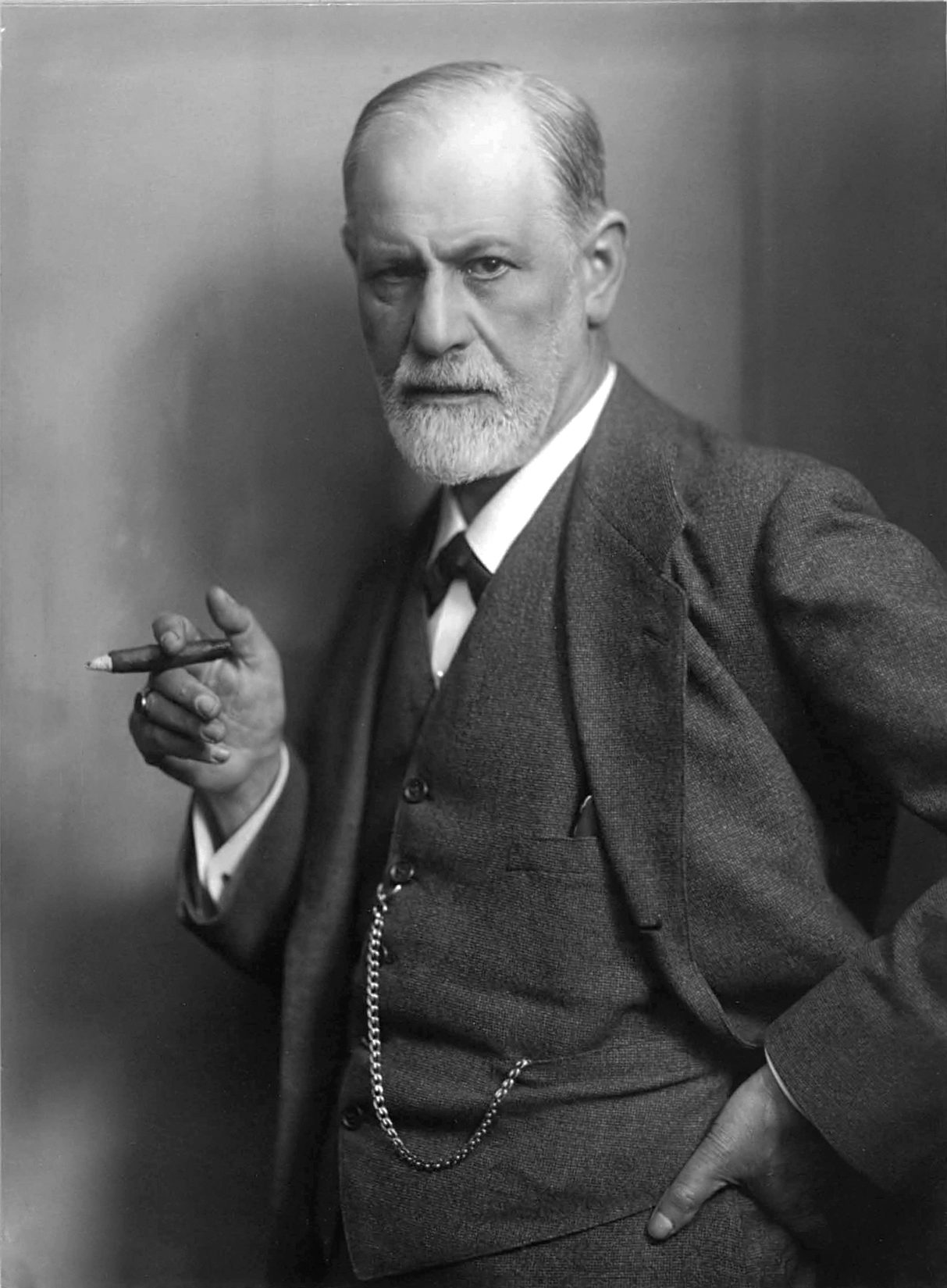 Retrato en blanco y negro de un hombre mayor con barba blanca recortada, traje de tres piezas y un puro en la mano derecha