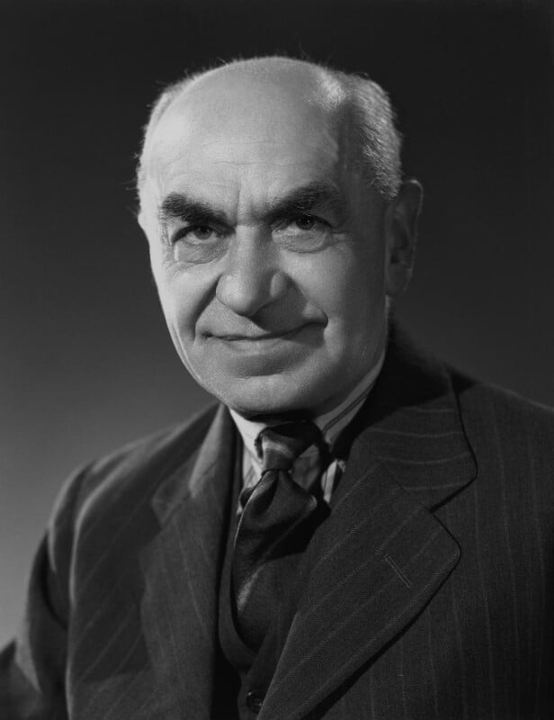 Retrato fotográfico en blanco y negro de un hombre mayor con traje y corbata, sonriendo levemente