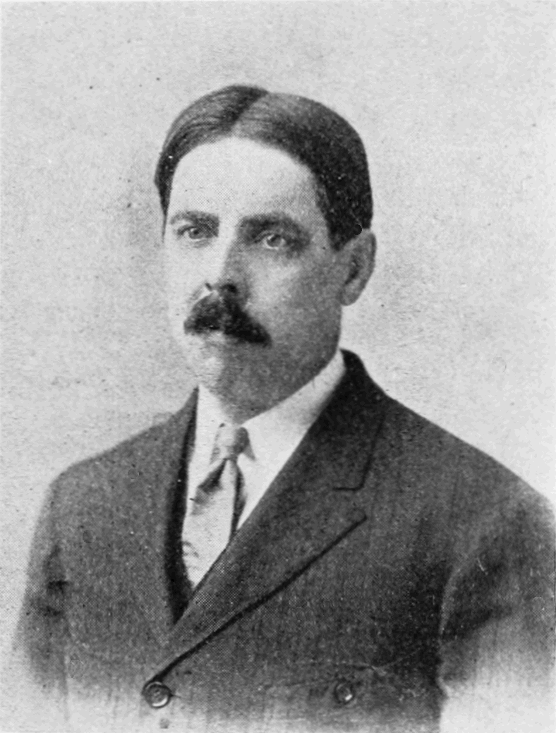 Retrato fotográfico en blanco y negro de un hombre de mediana edad con bigote, pelo con raya al lado, traje oscuro y corbata