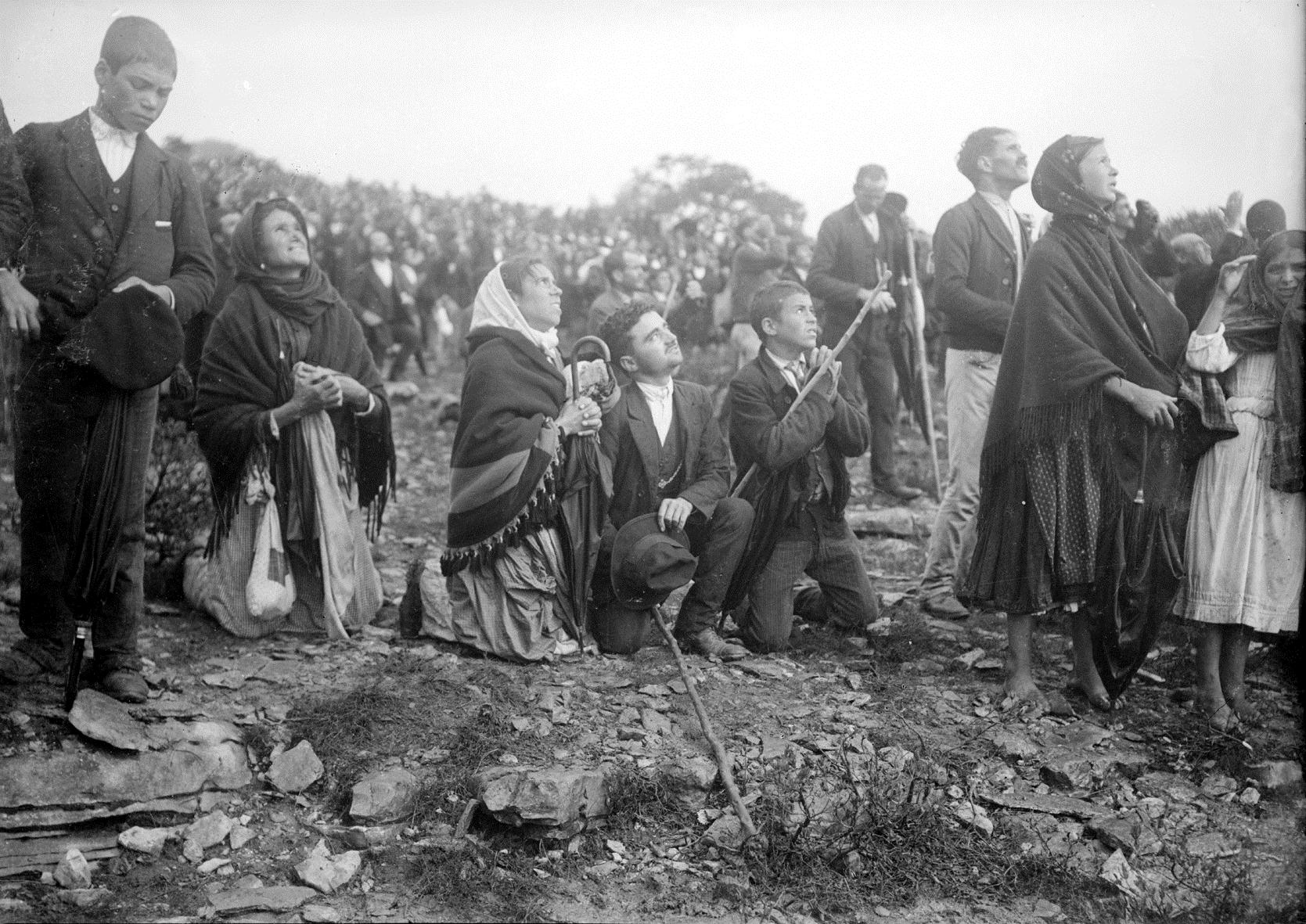 Fotografía en blanco y negro de un grupo de campesinos, hombres y mujeres, de pie y de rodillas, que miran hacia el cielo con expresión atenta