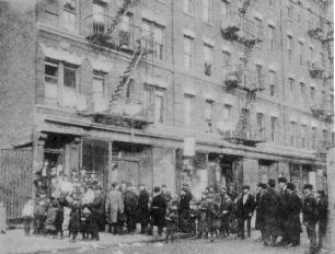 Fotografía antigua de una calle abarrotada del Lower East Side de Nueva York durante la huelga de alquileres de 1907, con una oradora dirigiéndose a los inquilinos