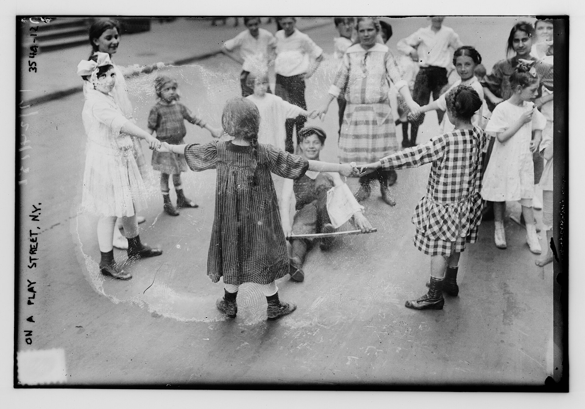 Fotografía antigua de un corro de niñas y niños jugando en una calle de Nueva York