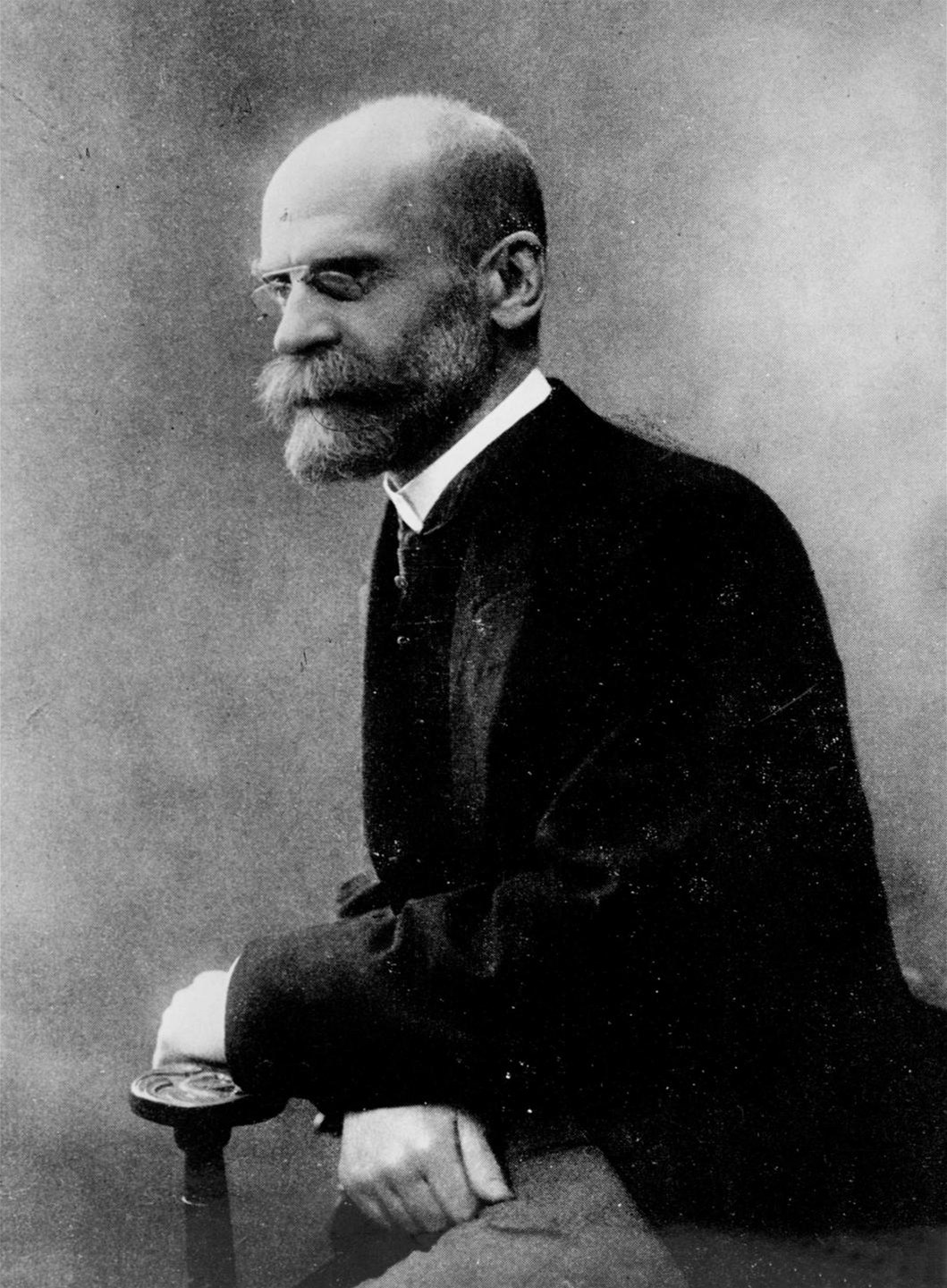 Retrato fotográfico en blanco y negro de un hombre con barba y bigote, sentado, con traje oscuro