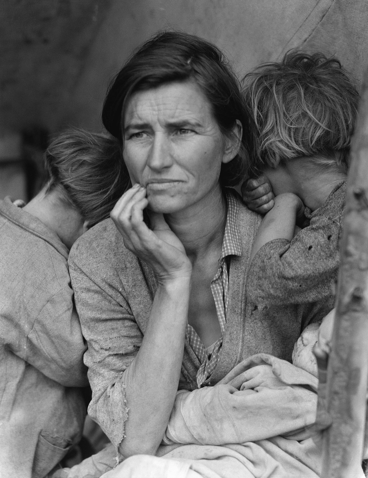 Fotografía en blanco y negro de una mujer de expresión preocupada, con la mano en la barbilla, junto a dos niños que esconden la cara en sus hombros y un bebé en su regazo