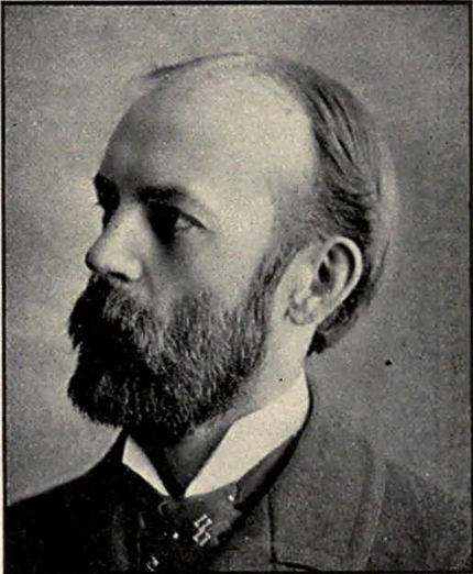 Retrato fotográfico en blanco y negro de un hombre calvo con barba poblada, visto de perfil, con chaqueta y corbata