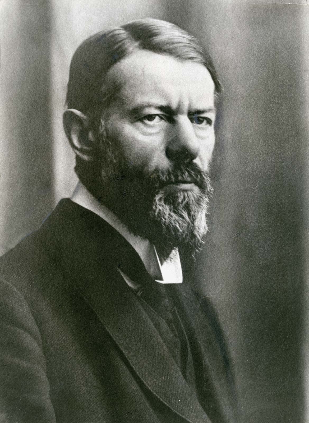 Retrato fotográfico en blanco y negro de un hombre de mediana edad con barba oscura, traje y corbata, mirando a un lado con expresión seria