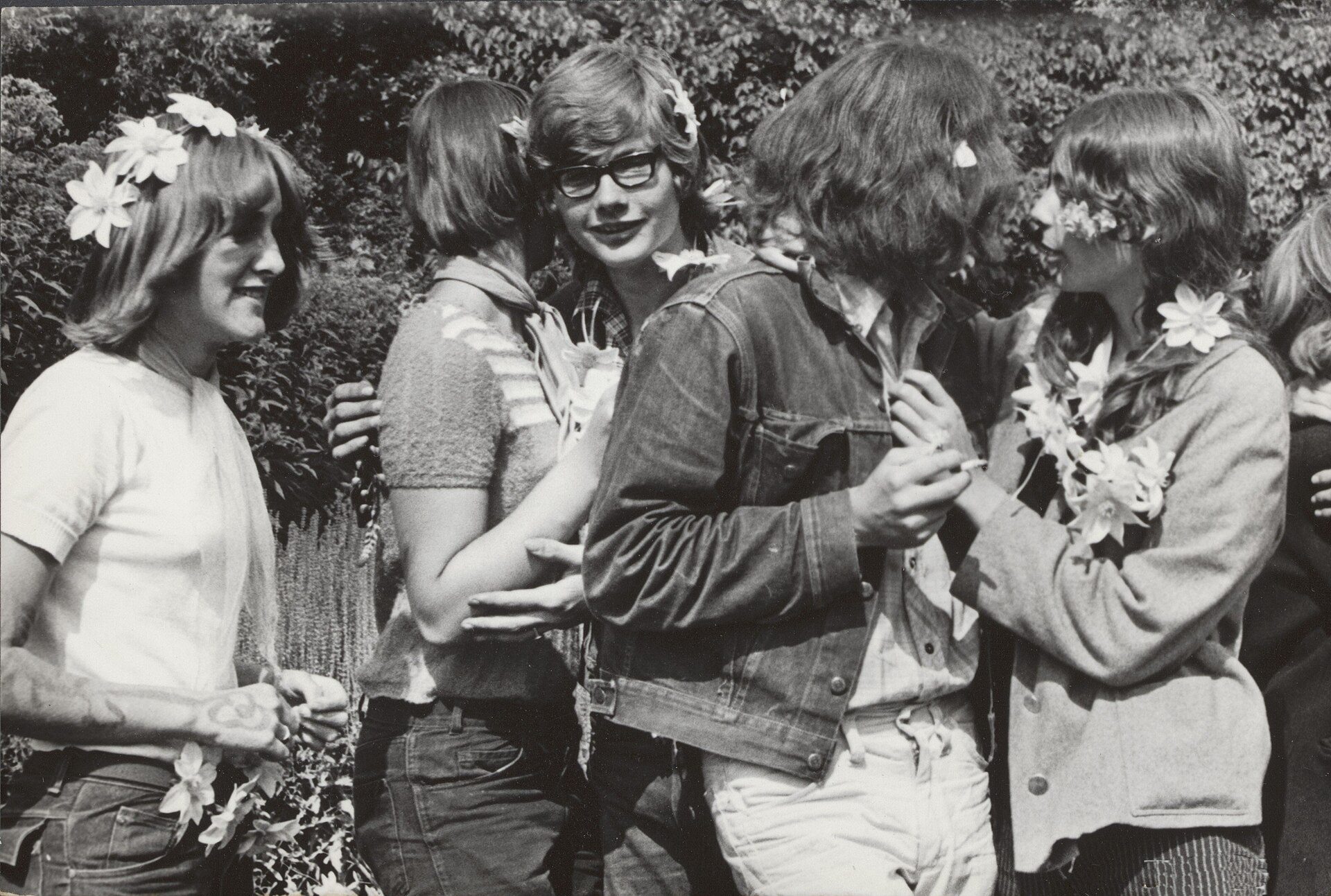 Fotografía de finales de los años sesenta de un grupo de adolescentes al aire libre con flores en el pelo, conversando