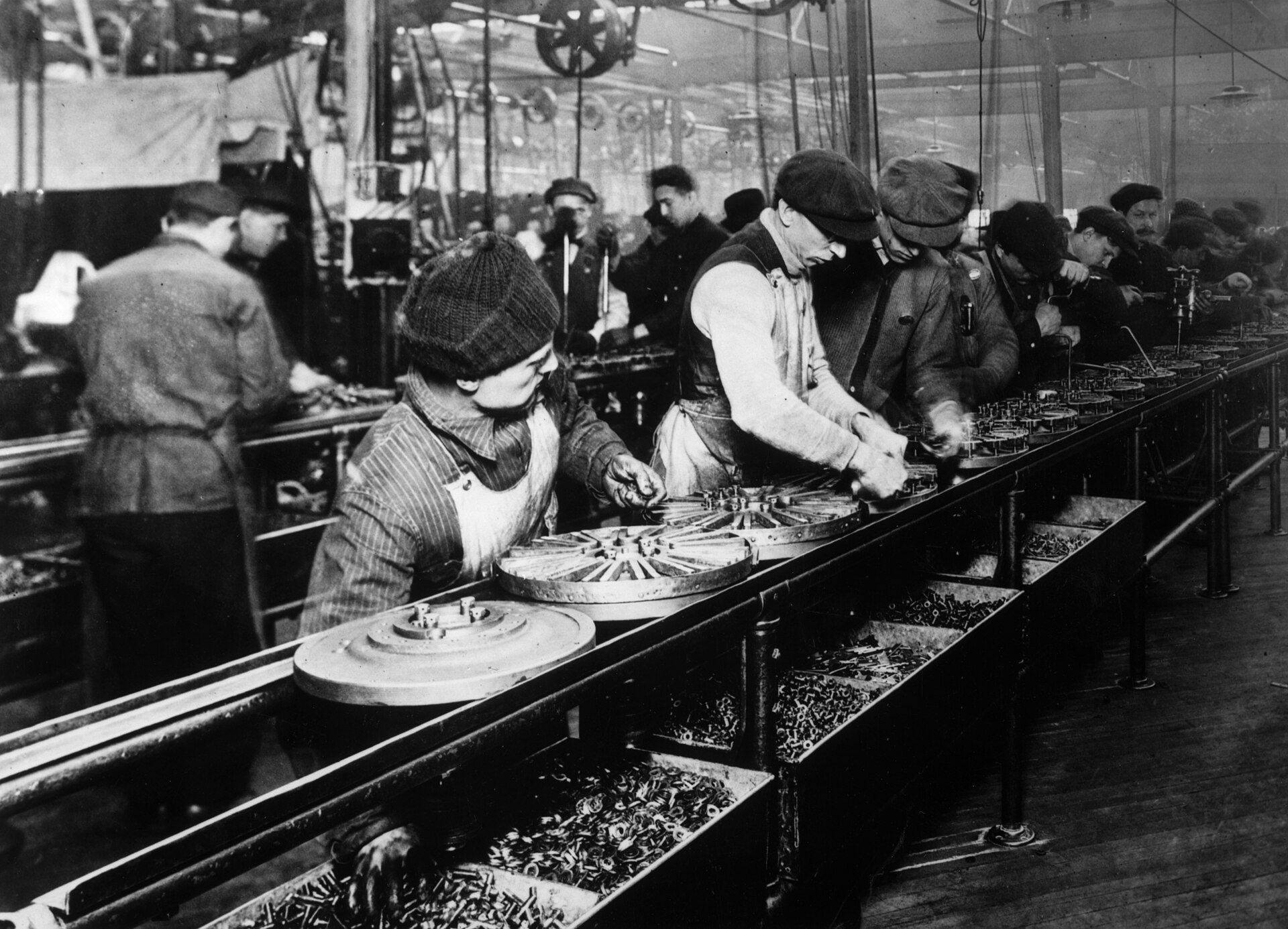 Fotografía de 1913 de una hilera de operarios inclinados sobre una cinta de montaje larga en una nave industrial