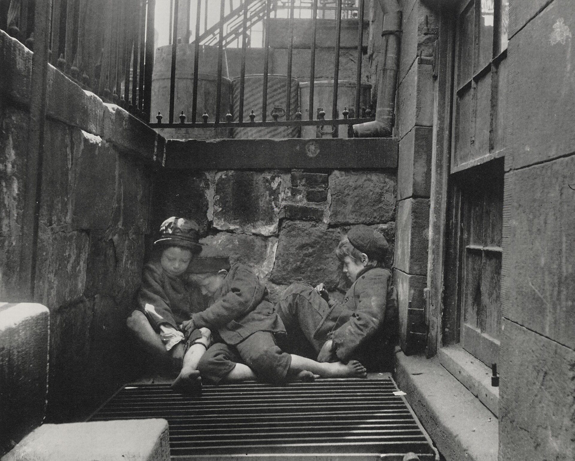 Fotografía de finales del siglo XIX de tres niños durmiendo acurrucados en un hueco de escalera de hierro en un callejón