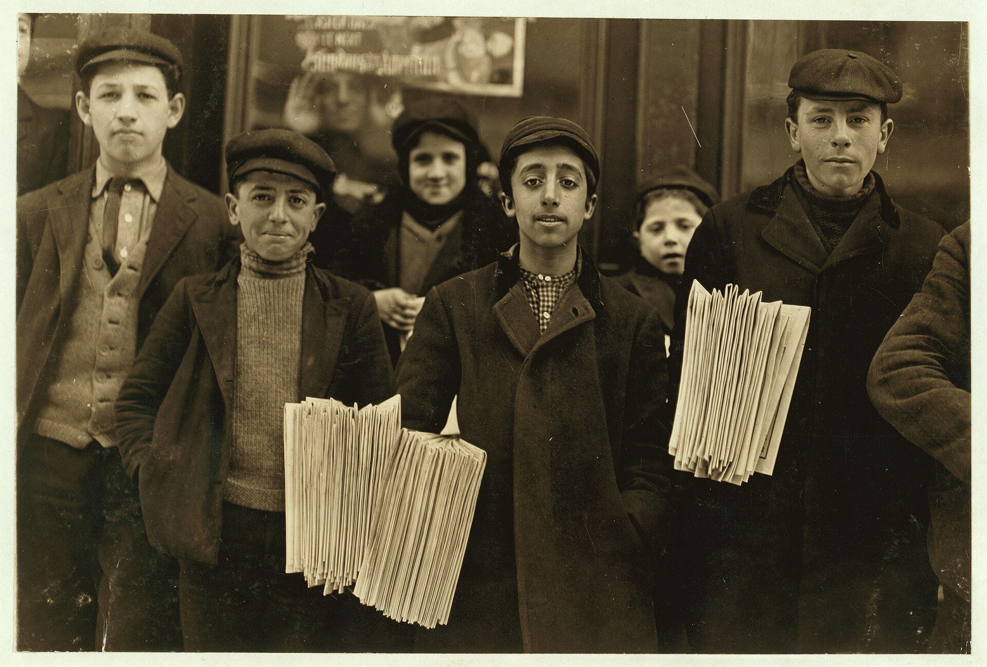 Fotografía de 1909 de un grupo de vendedores de periódicos adolescentes en una calle, mirando a cámara con los fajos de prensa bajo el brazo