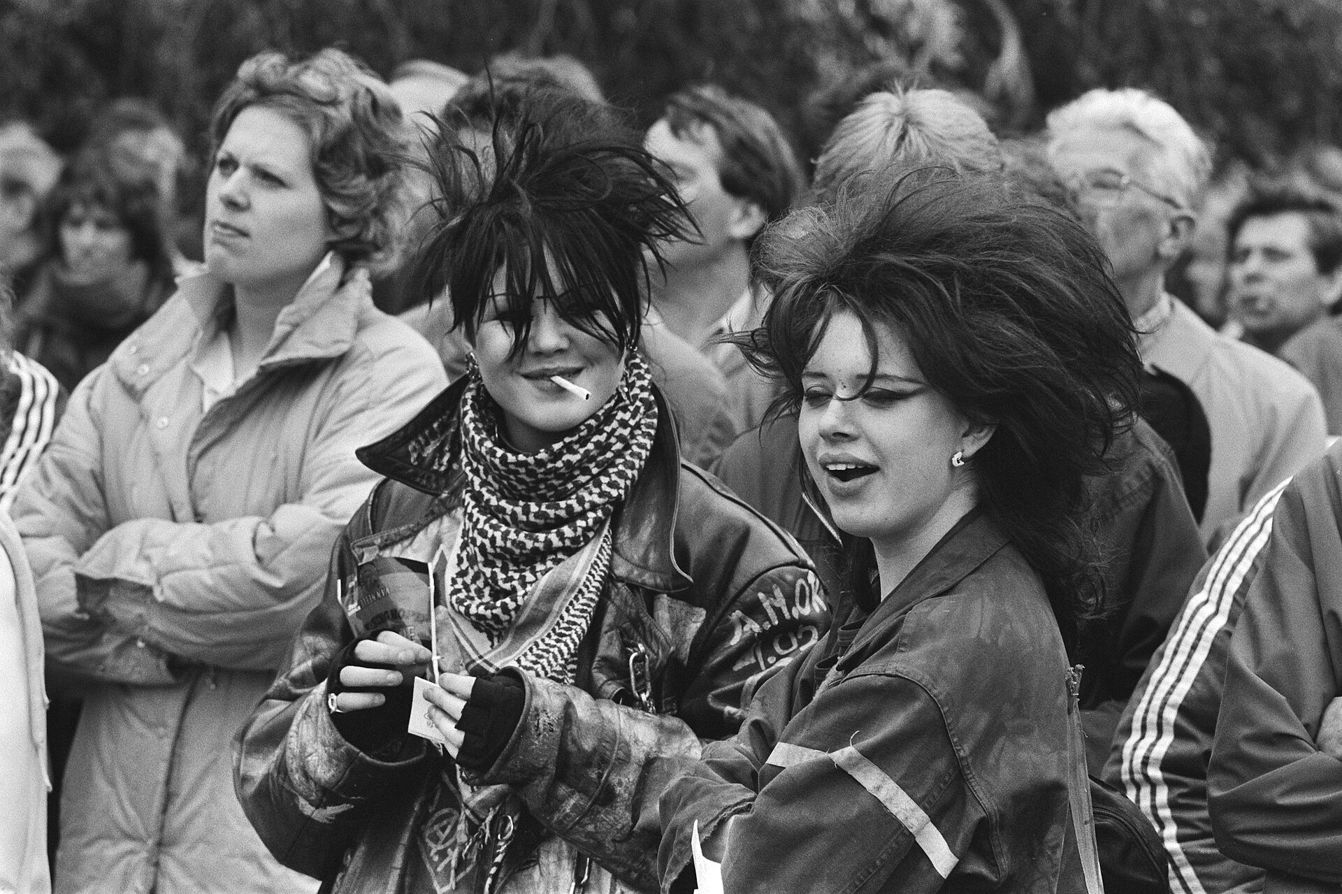 Fotografía de 1983 de dos chicas jóvenes con maquillaje oscuro y peinados punk en medio de un público adulto