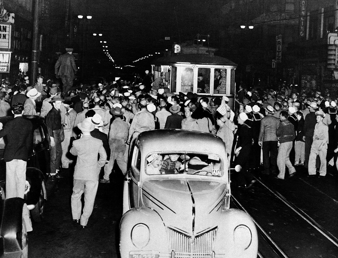 Fotografía nocturna de junio de 1943 con una multitud rodeando un tranvía y un automóvil en una calle céntrica iluminada
